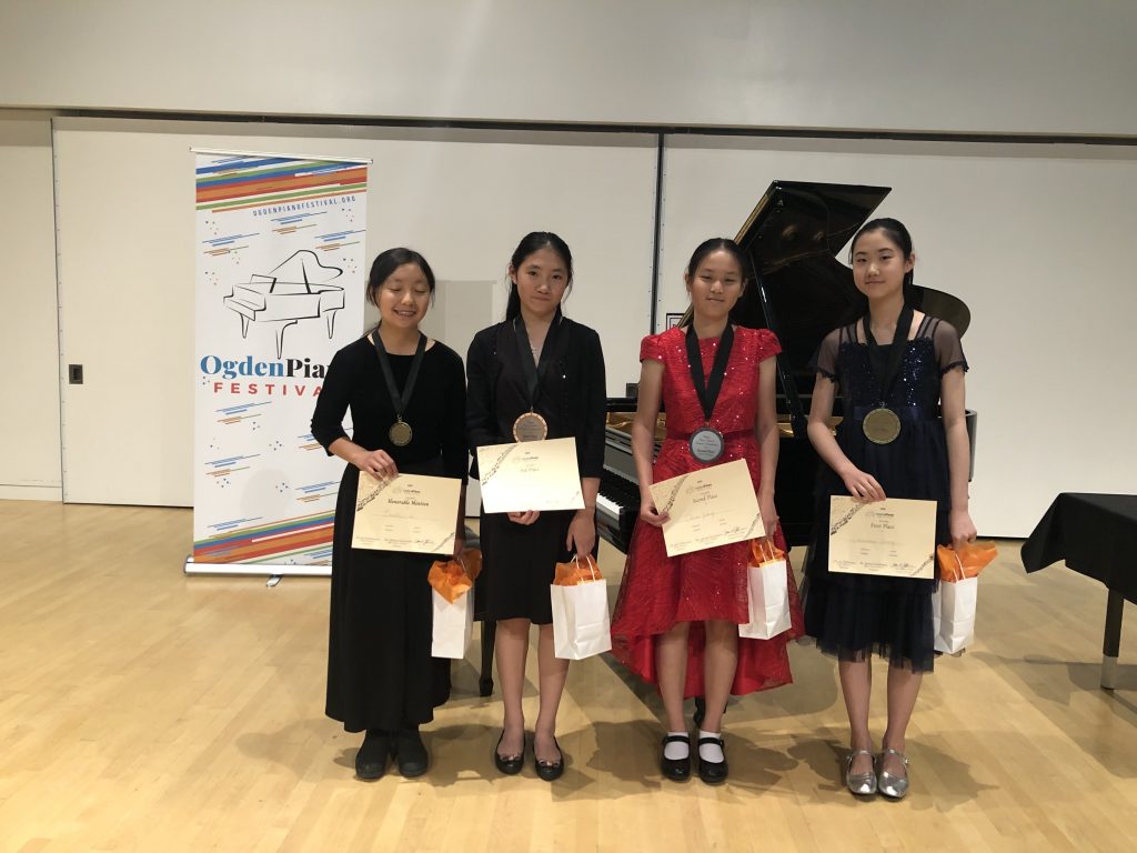 Junior Division Winners with gift bags and certificates in front of Ogden Piano Festival banner and Steinway Grand Piano