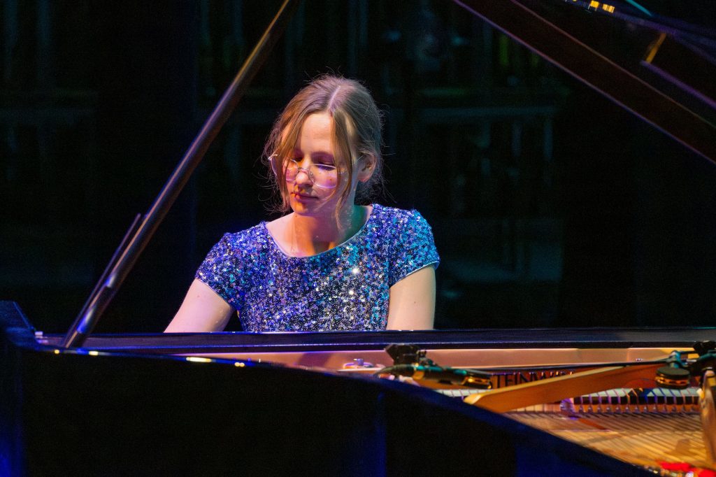 Emily Runov plays at the piano. View is across the body of the piano. 