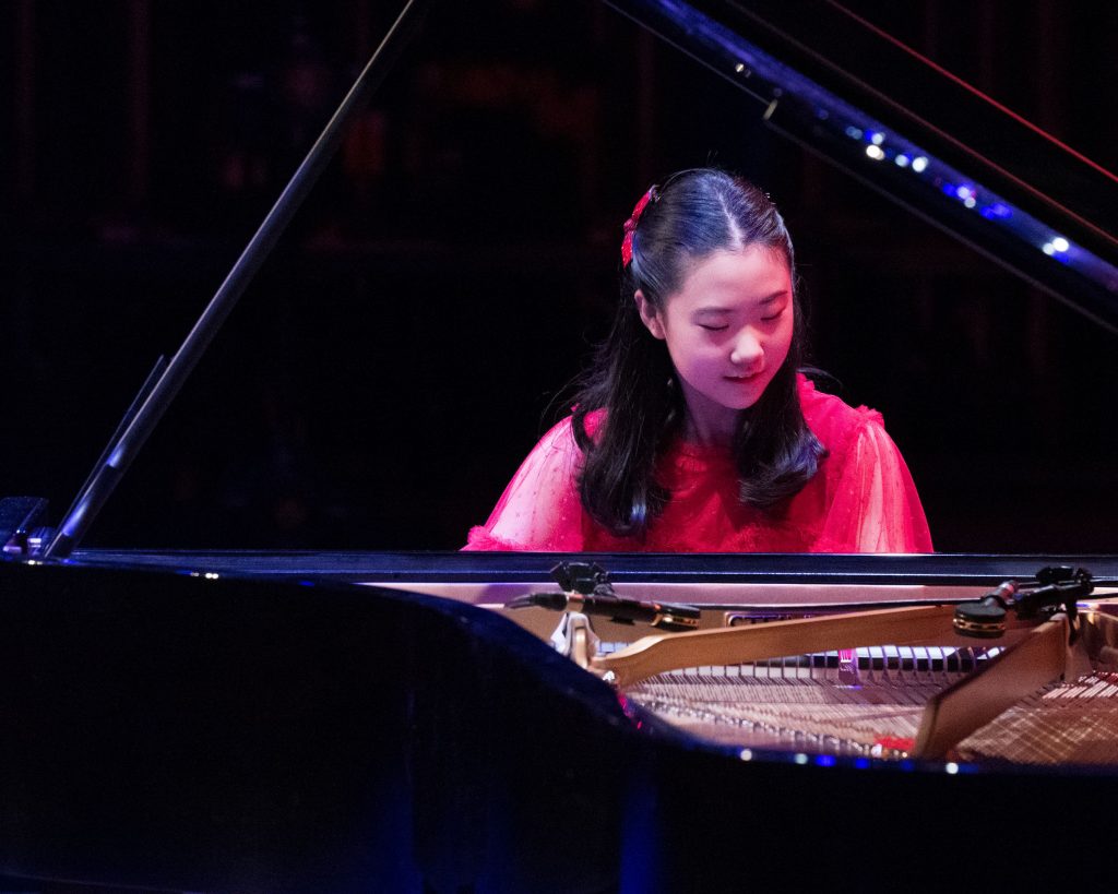 Christina Sung plays the piano. View is across the body of the piano with lid raised. 