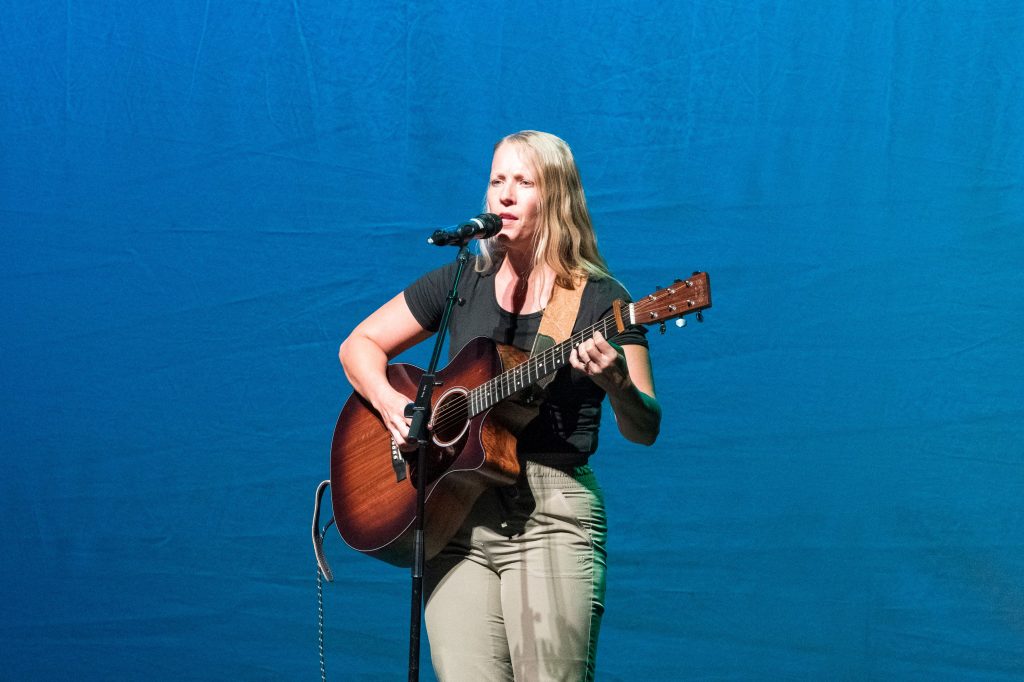 Sarah Jayne sings an original composition with her guitar onstage.