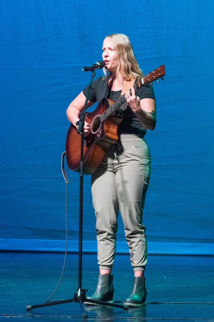 Sarah Jayne sings an original composition with her guitar onstage.