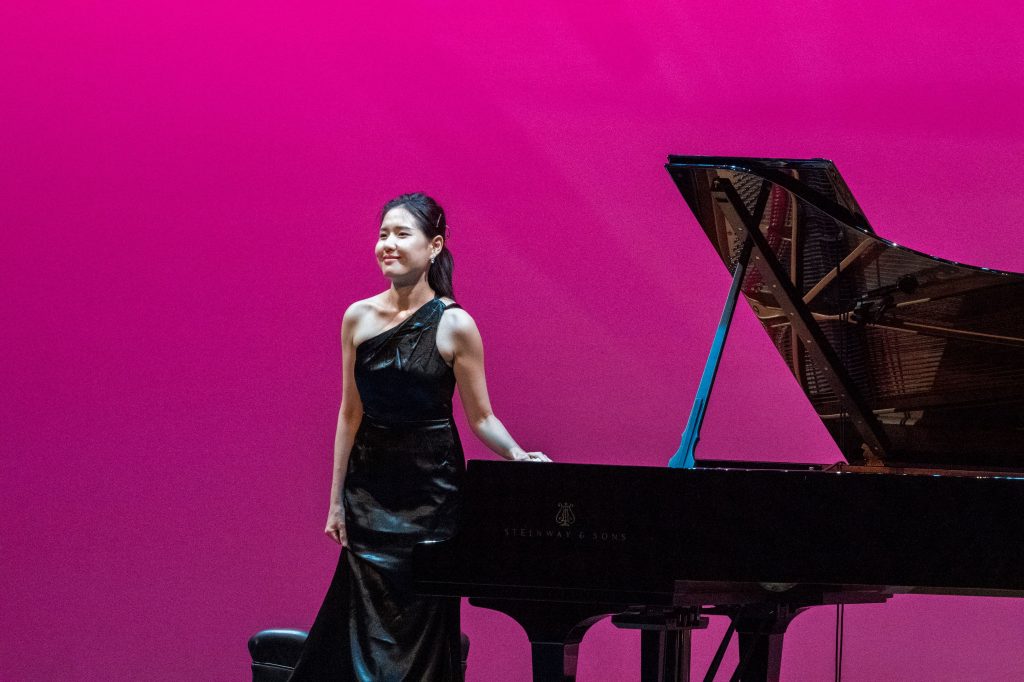 Dr. Esther Jeehae Ahn stands near piano to bow